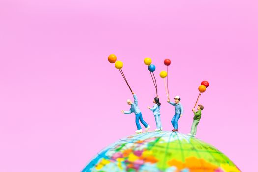 Miniature people : Happy family holding balloon on The globe with pink background and copy space for text