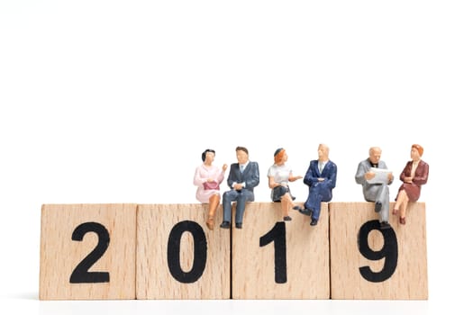 Miniature people sitting on wooden block number 2019. on white background