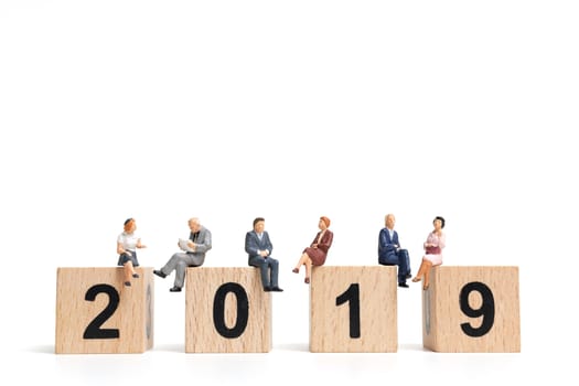 Miniature people sitting on wooden block number 2019. on white background