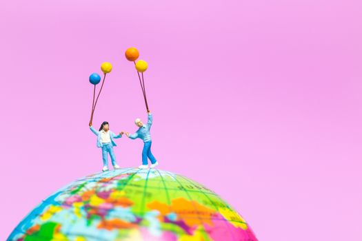 Miniature people : Happy family holding balloon on The globe with pink background and copy space for text