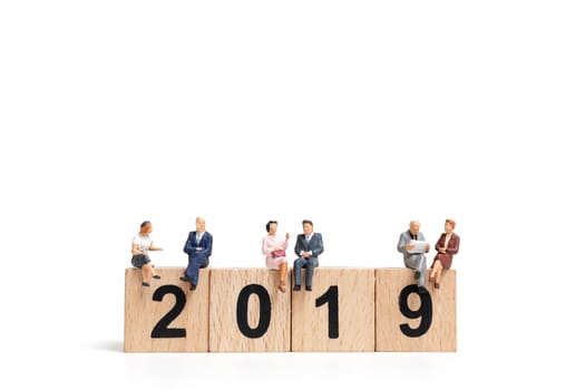 Miniature people sitting on wooden block number 2019. on white background