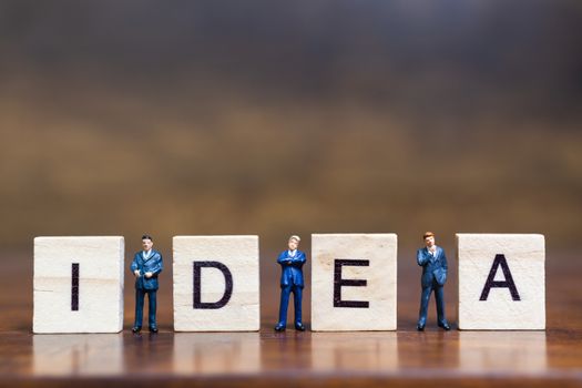 Miniature people standing with wooden block " Idea " words on wooden background