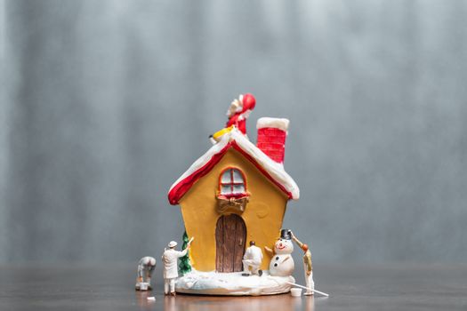 Miniature people painting house and Santa Claus sitting on the roof , Merry Christmas and happy holidays concept.