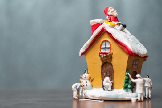 Miniature people painting house and Santa Claus sitting on the roof , Merry Christmas and happy holidays concept.