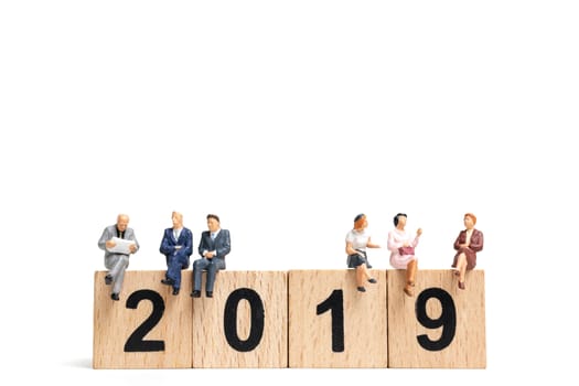 Miniature people sitting on wooden block number 2019. on white background