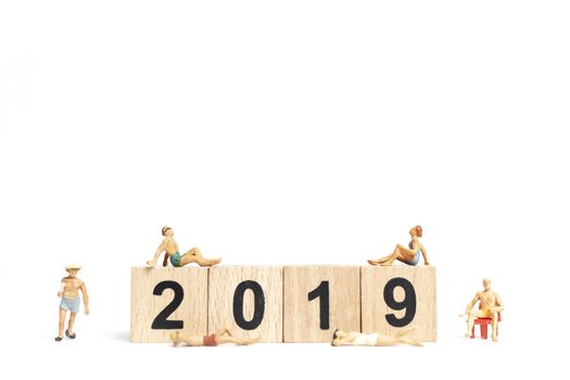 Miniature people wearing swimsuit relaxing on wooden block 2019 with white background