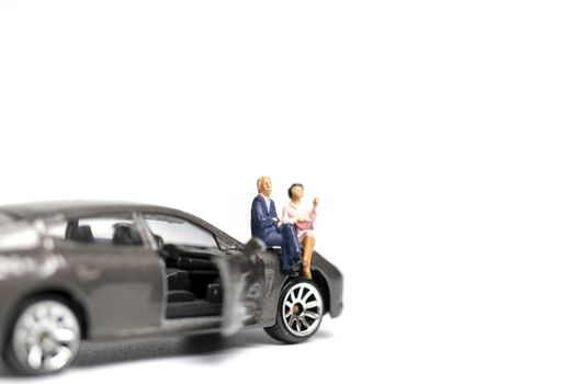 Miniature people sitting on car with copy space on white background 