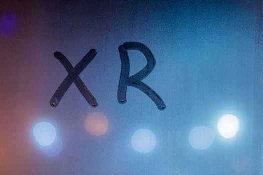 an abbreviation xr for extended reality handwritten on blue night wet window glass.