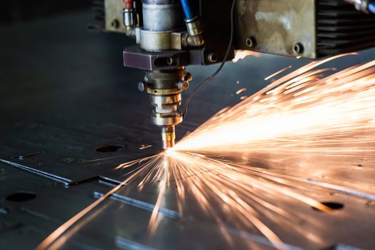 laser cutting process with a sheaf of sparks and motion blur of head unit while piercing through zinc plated steel sheet, close-up with selective focus and background blur