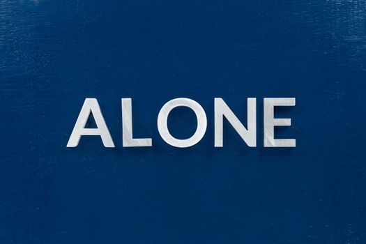 The word alone laid with silver metal letters in center of painted classic blue flat board. View directly from above in flat lay perspective.