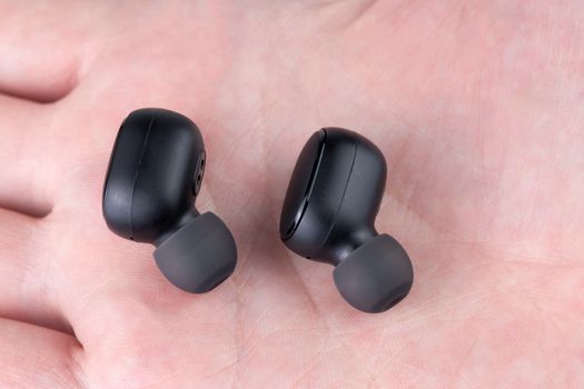 a pair of black wireless bluetooth earbuds laying on caucasian palm - close-up with selective focus