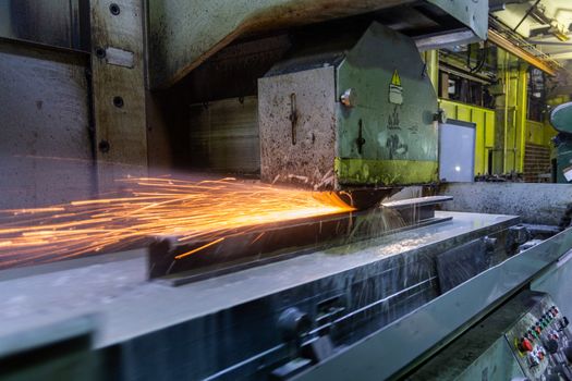 a process of flat surface grinding with a lot of sparks and liquid cooling indoors at metalworking shop, old factory equipment at work