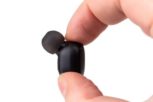 two caucasian fingers holding a black wireless earbud - close-up with selective focus, isolated on white background