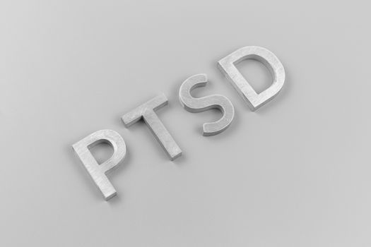 an abbreviation PTSD - post traumatic stress disorder - laid with silver metal letters on light grey flat surface in ascending diagonal composition