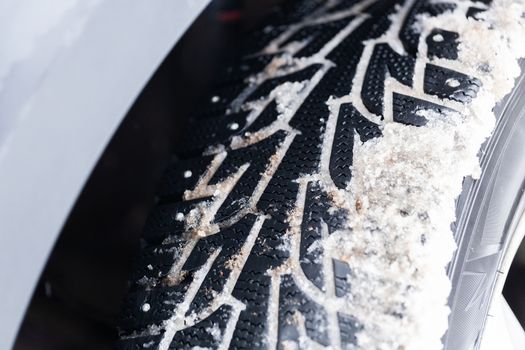 an unadorned picture of winter car wheel with metal spikes on snow close-up.