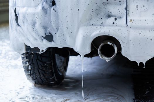 a fossil fuel car covered by soap foam while washing indoors - close-up low angle view from back with selective focus.