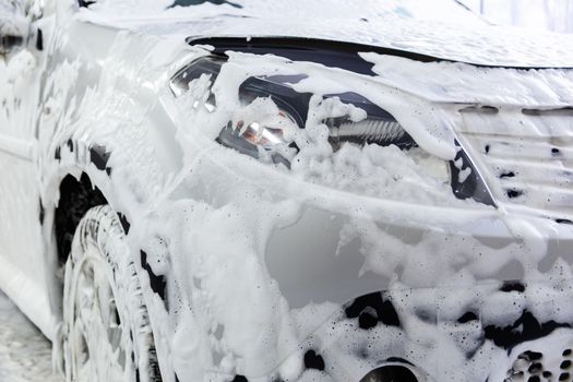 a car covered by soap foam while washing indoors - close-up wiew with selective focus.