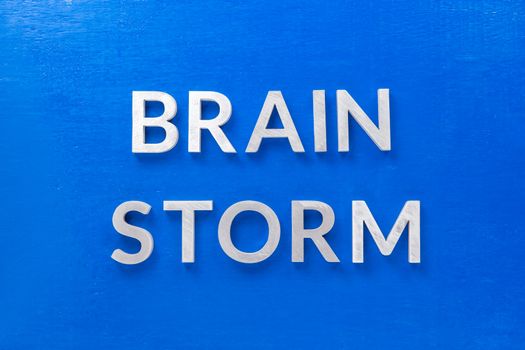 the phrase brain storm laid with silver metal letters on blue board in flat lay with central composition.