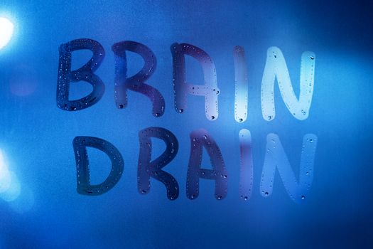 the word brain drain written on night wet window glass close-up with blurred background in classic blue color.