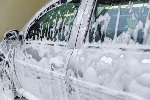 a car covered by soap foam while washing indoors - close-up with selective focus.