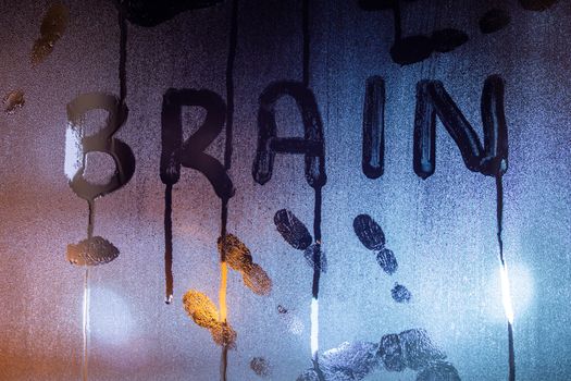 the word brain written on night wet window glass with palm prints close-up with blurred background.