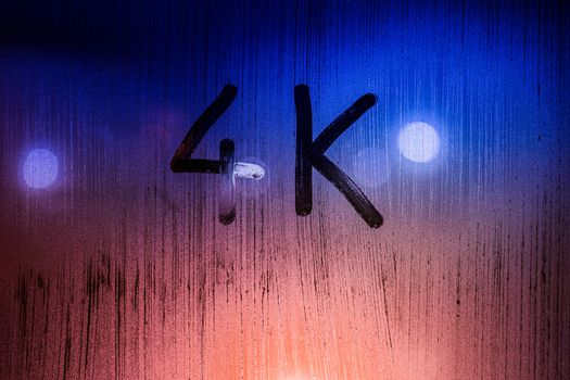 The word 4k handwritten on wet glass with blurred night lights in background.