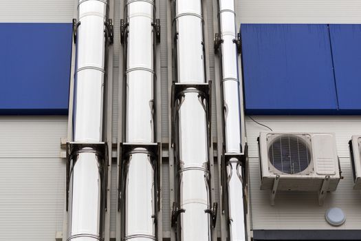 Chrome ventilation pipes on the outside wall of the white and blue Industrial building.