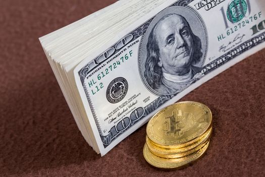a bunch of us dollar banknotes and three bitcoin shiners on brown fleece background close-up with selective focus.