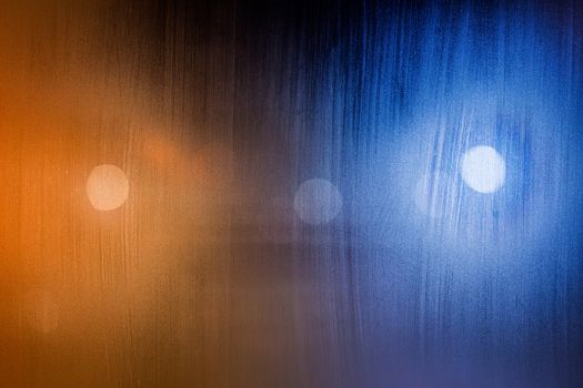 an abstract background of foggy wet window glass at night with blurry street lights.
