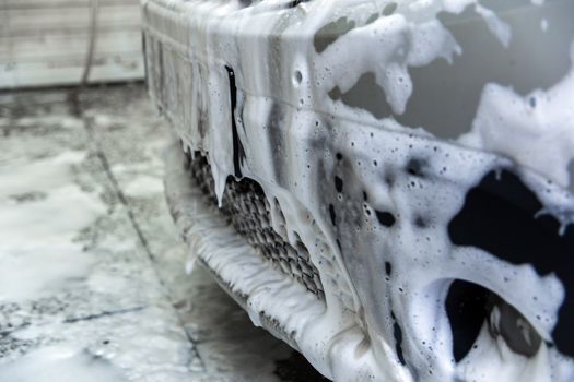 a nose of car covered by soap foam while washing indoors - close-up front wiew with selective focus.