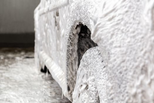 a car covered by soap foam while washing indoors - close-up with selective focus.
