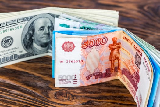 a two bunches of russian rubl and us dollar banknotes standing on brown wood surface close-up with selective focus and blur