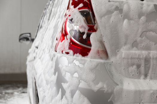 a car covered by soap foam while washing indoors - close-up wiew from back with selective focus.