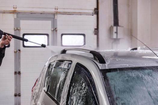 Indoor self car washing. Process of removing soap foam from roof of vehicle with high pressure water stream - close-up vith selective focus and motion blur.