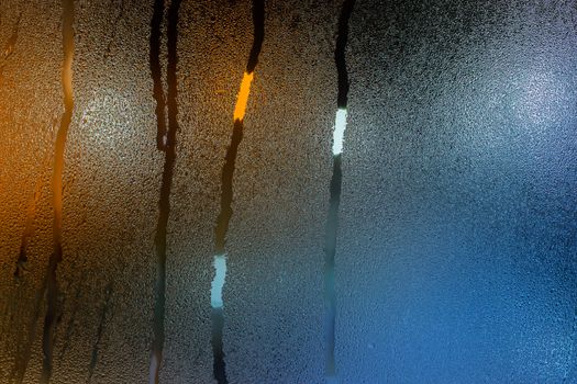 an abstract background of night wet window glass with smudges in teal-orange tone gamma.