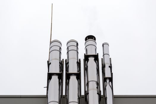 Chrome ventilation pipes on the outside wall of the white and blue Industrial building.