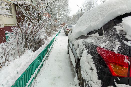 Parked cars covered by thick snow layer after winter blizzard at cloudy day light,