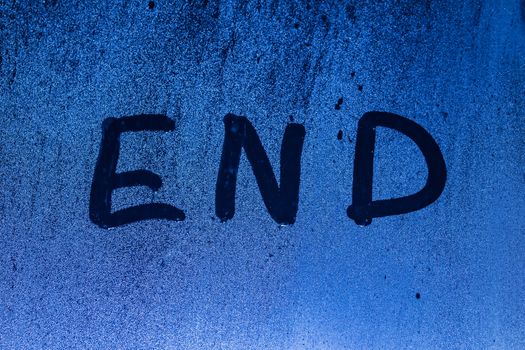 The word end written on night sweaty window glass with blurred blue light in the background.