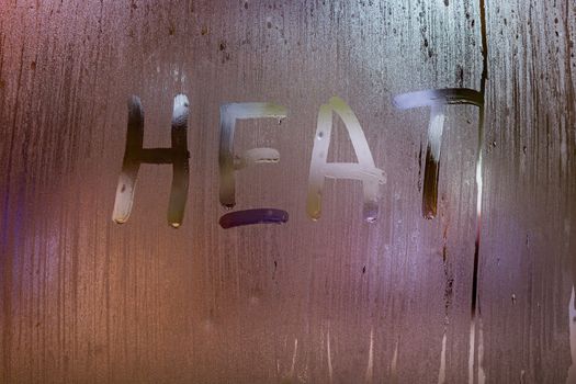 the word heat written on night wet window glass close-up with bokeh background.