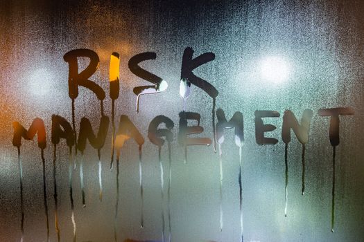 the word risk management handwritten on night wet window glass with many smudges