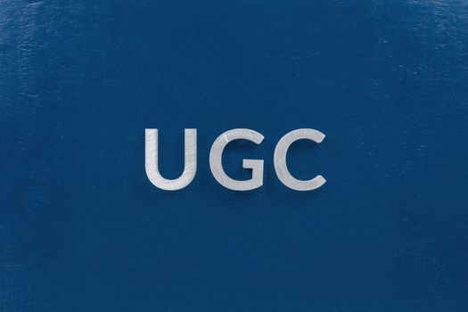 the word ugc - user generated content - laid by white silver metal letters on classic blue background in flat lay central composition.