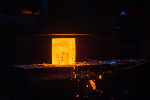 close-up picture of hot steel manual forging process with big mechanical hammer machine, sparks flying out from workpiece