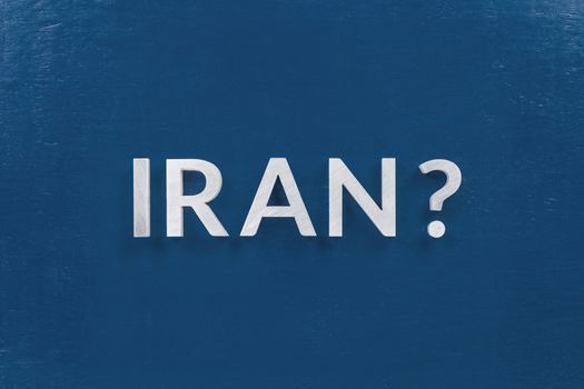 a question iran laid with silver metal letters on classic blue board in flat lay with central composition.