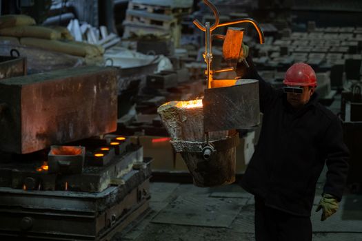 Worker moving metallurgical ladle with molten steel with crane before form filling. Industrial chill casting in old factory,