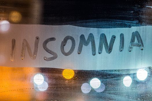 the word insomnia written on night wet window glass close-up with blurred background.
