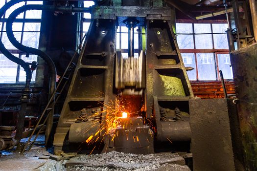 old working steam hammer at factory forging hot steel workpiece with sparks.