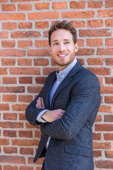 Smart casual businessman on urban city brick wall background lifestyle portrait. Young professional man smiling confident in blazer. Career and entrepreneurship concept.