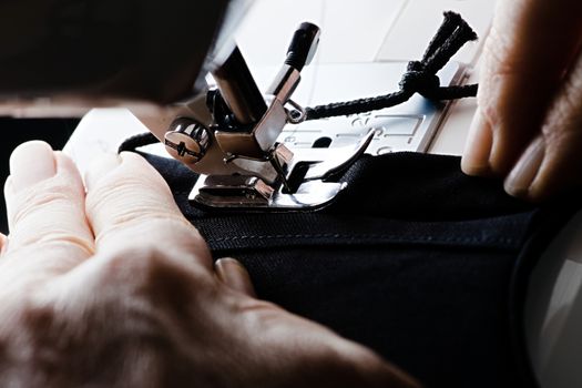 From right to left, a seam is stitched on a black homemade face covering or face mask. Guided by older weathered hands.