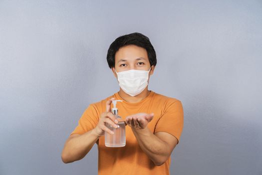 Asian man wearing face surgical mask presenting and using alcohol gel or hand sanitizer on blue color background, covid19 outbreak and pandemic,healthcare and protection against virus concept