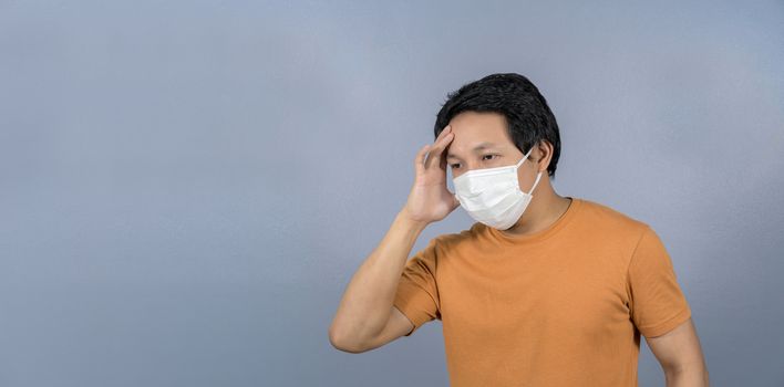 Asian man wearing face surgical mask Headache and worry on blue background, Coronavirus pandemic, covid19 outbreak, social distancing and responsibility,healthcare and protection against virus concept